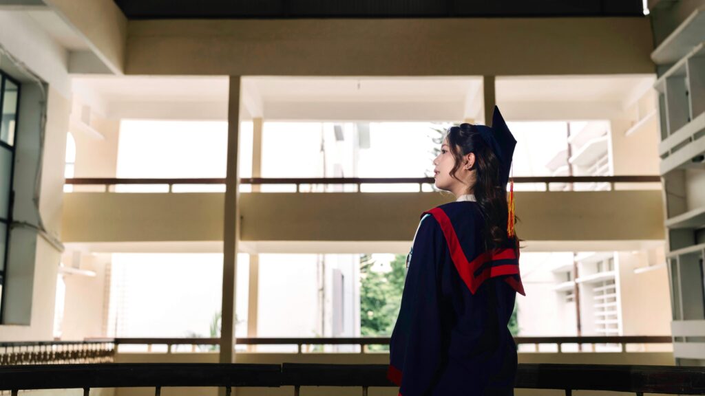 Side view of a young graduate in cap and gown in a school hallway.